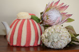 By the Tea Cosy Project - Hand knit tea cosy in protea colours, mostly pink and beige striped with an added green flower.