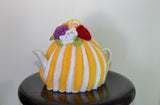 By the Tea Cosy Project - Hand knit tea cosy in bright yellow and white striped colours with bright flowers to finish on top.